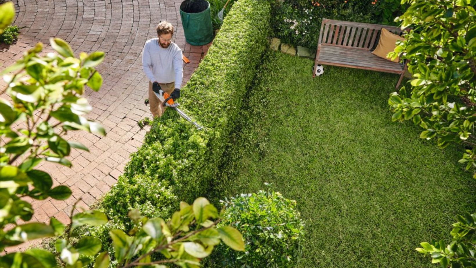 a man trimming the top of a hedge