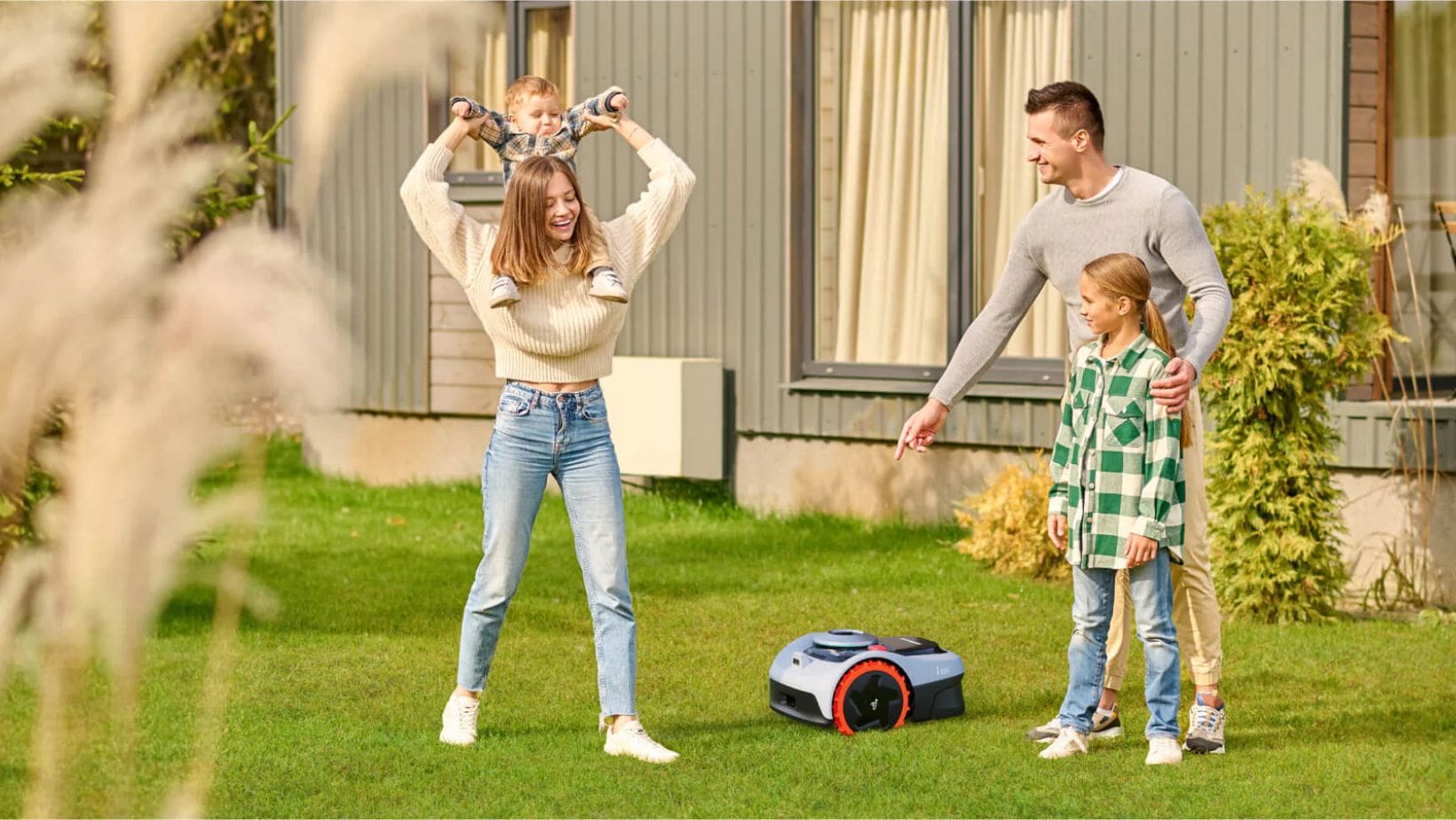 a father, his 3 children and a robotic lawn mower in a garden