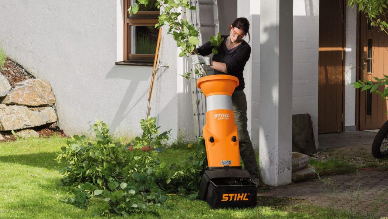 a woman getting rid of tree branches and green garden waste into a STIHL GHE 150 Electric Chipper