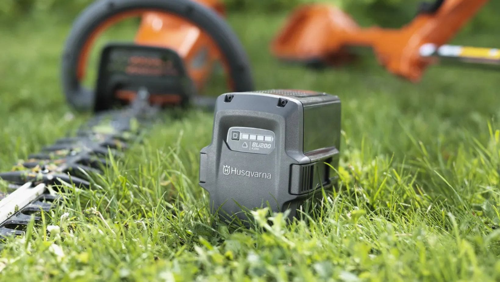 a Husqvarna battery and 2 cordless garden tools laid on grass