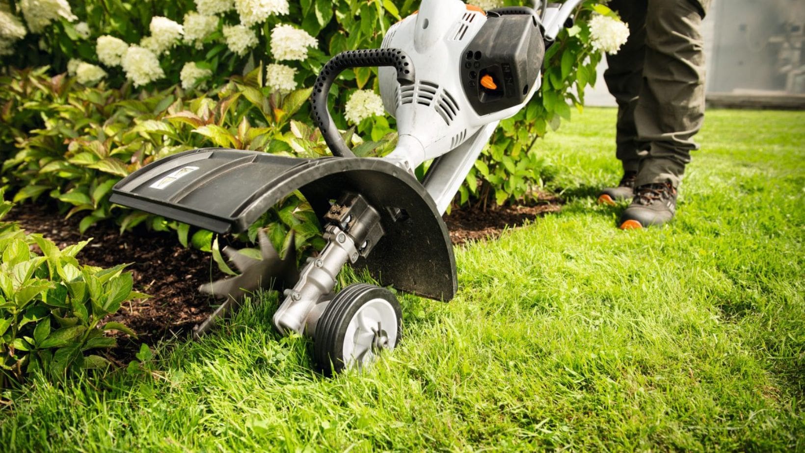 someone using a lawn edger where a lawn meets a flowerbed