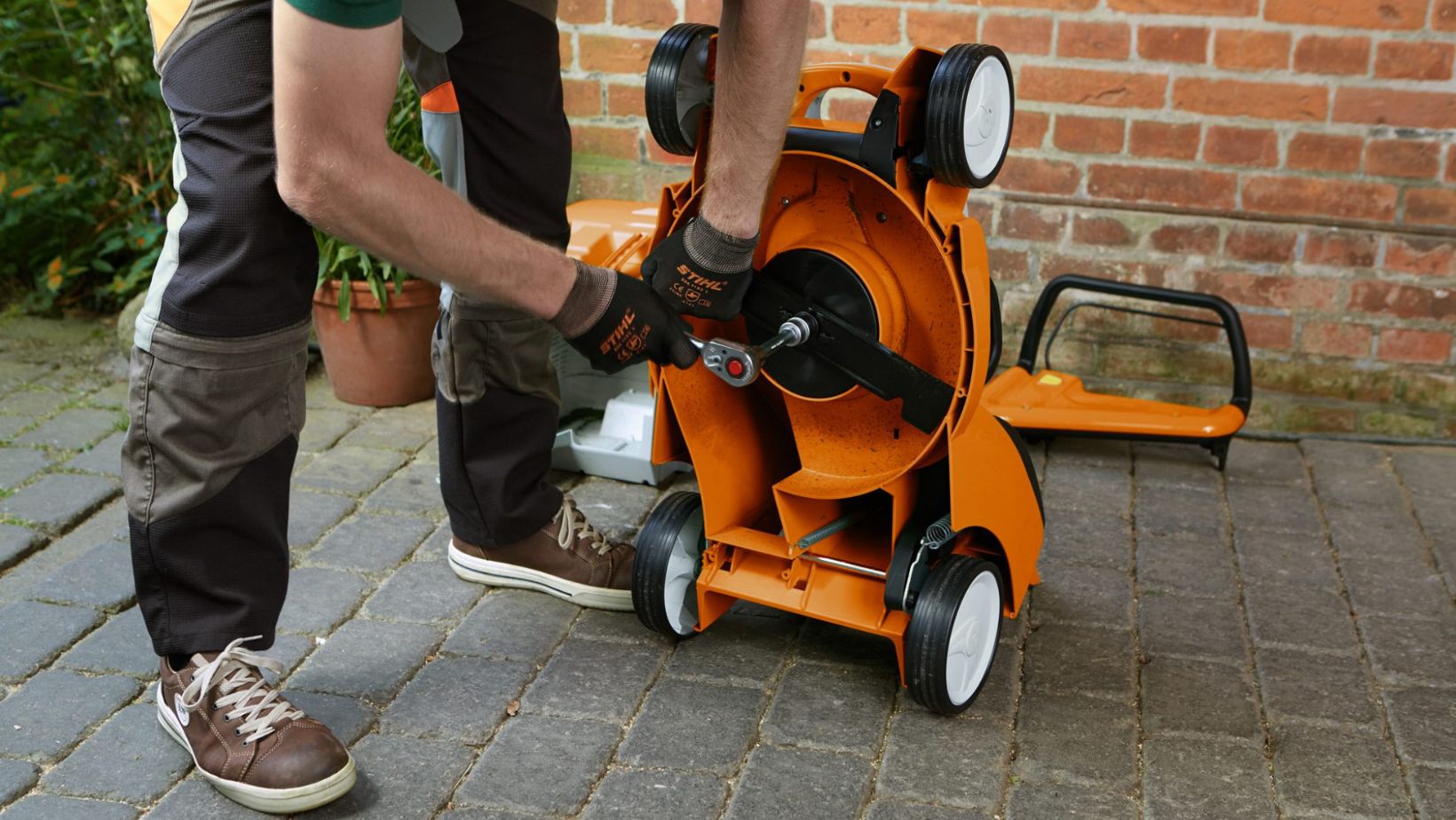 a man using a spanner to remove a lawnmower blade on an orange STIHL mower